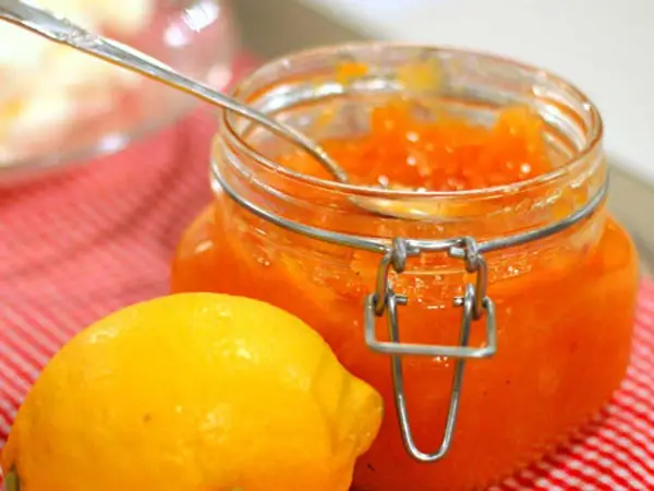 En burk med hemgjord citronmarmelad och en färsk citron på en rödvitrutig duk.