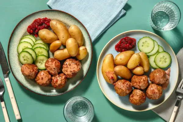 Två tallrikar med köttbullar, småpotatis, gurka och lingonsylt. En perfekt snabb middag för två.